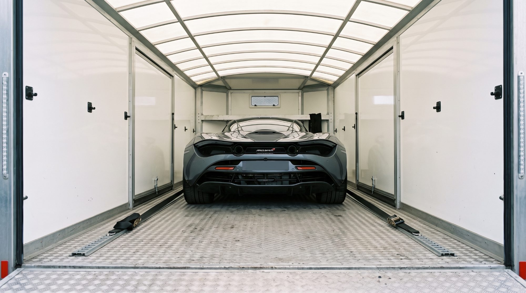 Inside the bright enclosed trailer, the car strapped by the wheels (concept image)